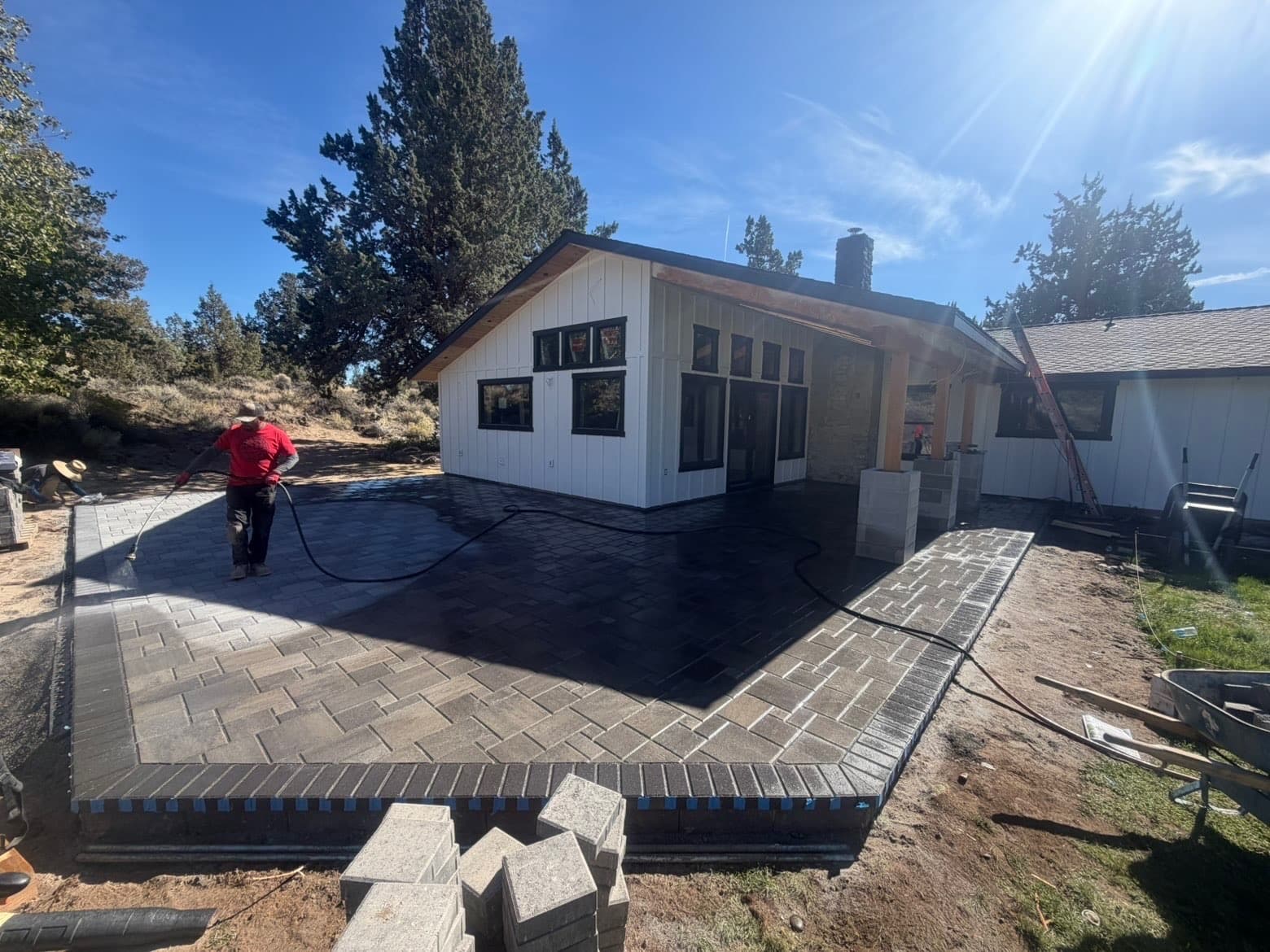 Wide view of the same back patio showing the paver pattern and border, with workers and stacked blocks during installation.