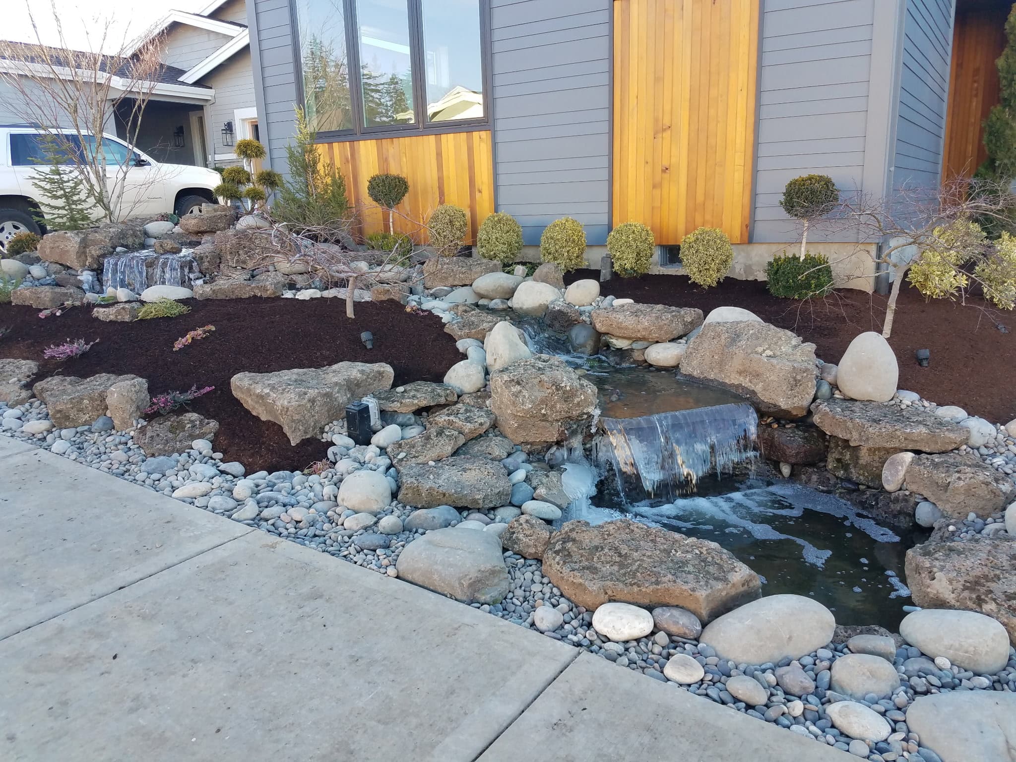 A finished rock water feature with two cascades beside a home.